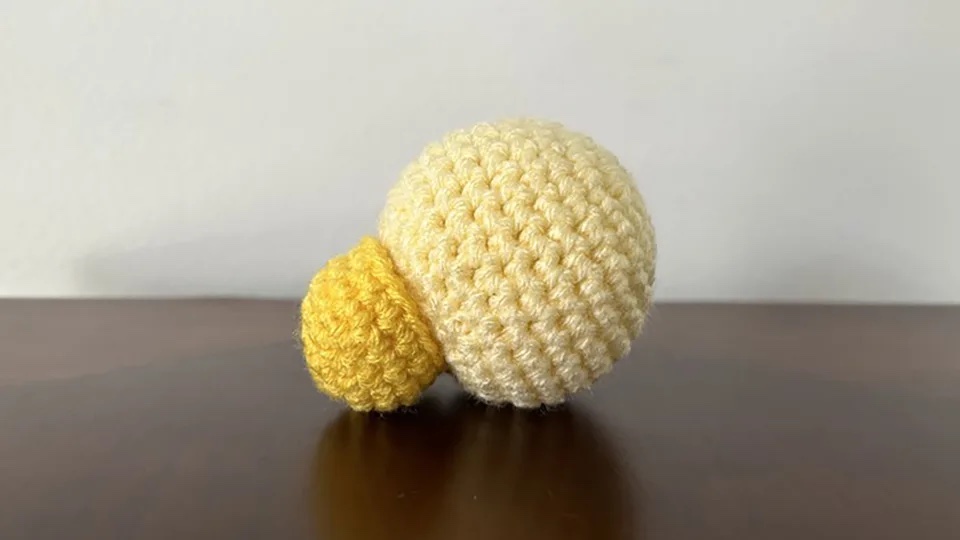 a crocheted object consisting of a light yellow sphere stuck to a smaller medium yellow sphere